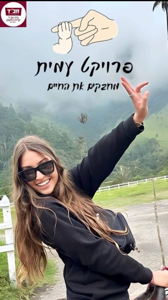 עמית מחייכת, לצידה כרזת ״פרויקט עמית — מחבקים את החיים״