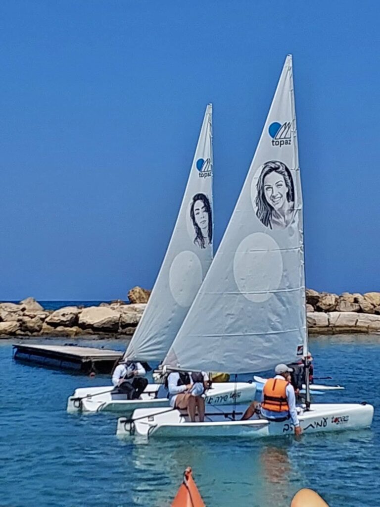 שתי סירות מפרש בים, ועל כל מפרש דיוקן ושם — של עמית ושל שירה אילון
